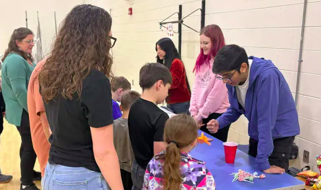 Three members standing behind a table showing kids how to use a 3D printed mechanical hand